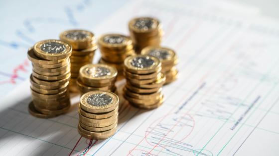 Stack of pound coins on financial graphs and figures