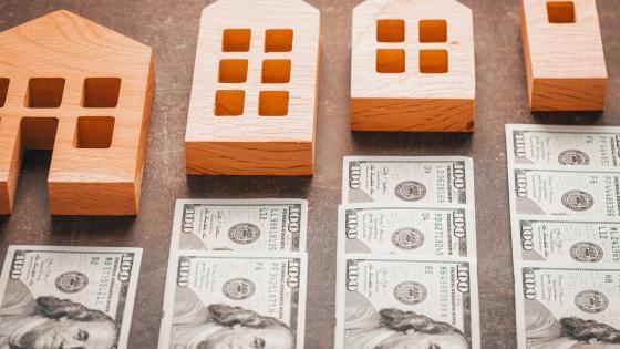 Dollar bills lined up between increasing small wooden houses